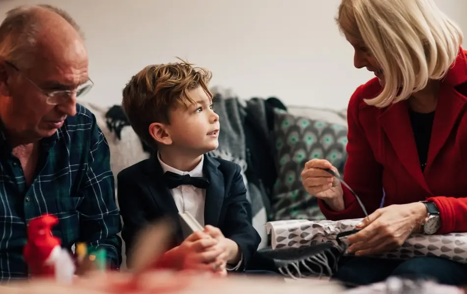 Ung gutt sitter i finstasen mellom sine besteforeldre, hvor bestemor pakker opp julegave