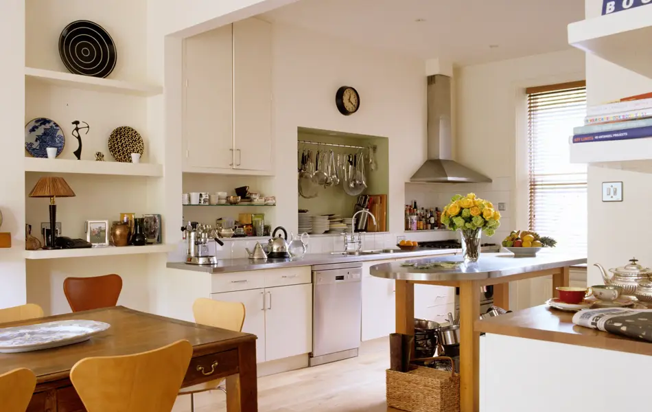 Kjøkken med hyller med vaser og mønstrete tallerkener, samt kokebøker og avis på benken 