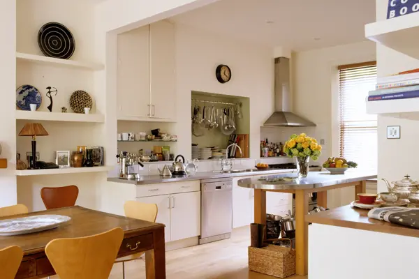 Kjøkken med hyller med vaser og mønstrete tallerkener, samt kokebøker og avis på benken 