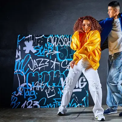 to ungdommer i trendy klær som danser foran en vegg med graffiti