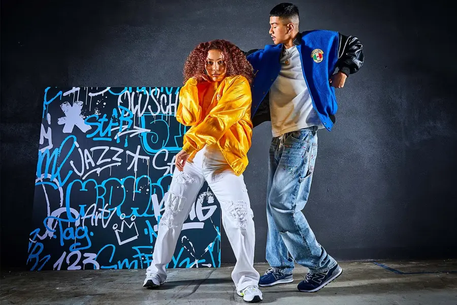 to ungdommer i trendy klær som danser foran en vegg med graffiti