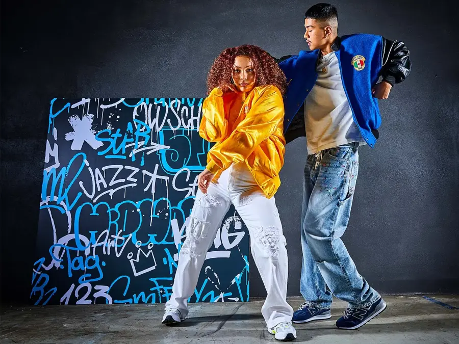 to ungdommer i trendy klær som danser foran en vegg med graffiti