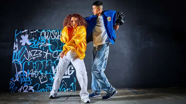 to ungdommer i trendy klær som danser foran en vegg med graffiti