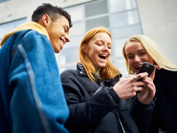 ungdommer som ser på telefon påkledd allværsjakke og denimjakke