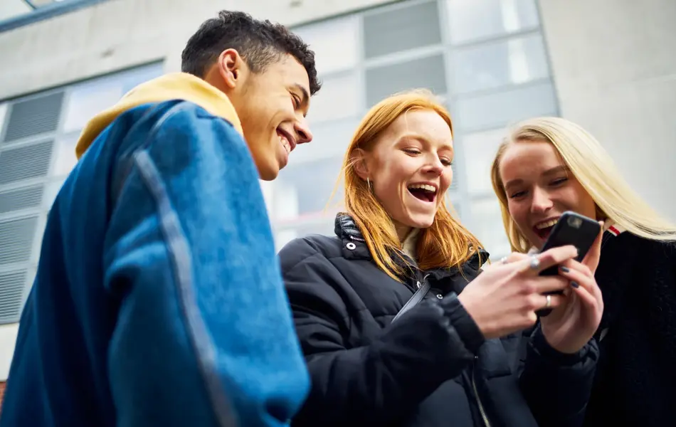 ungdommer som ser på telefon påkledd allværsjakke og denimjakke