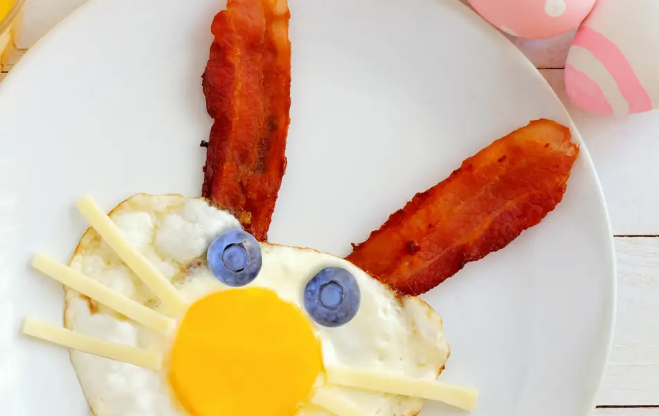 Easter breakfast with cute bunny face made of egg and bacon. Table scene, above view over a white wood background.