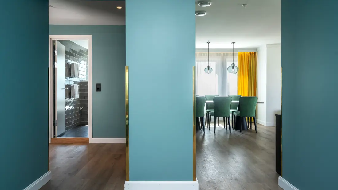 Grønn vegg, spisebord, 6 grønne stoler, vindu, gule gardiner, parkettgulv