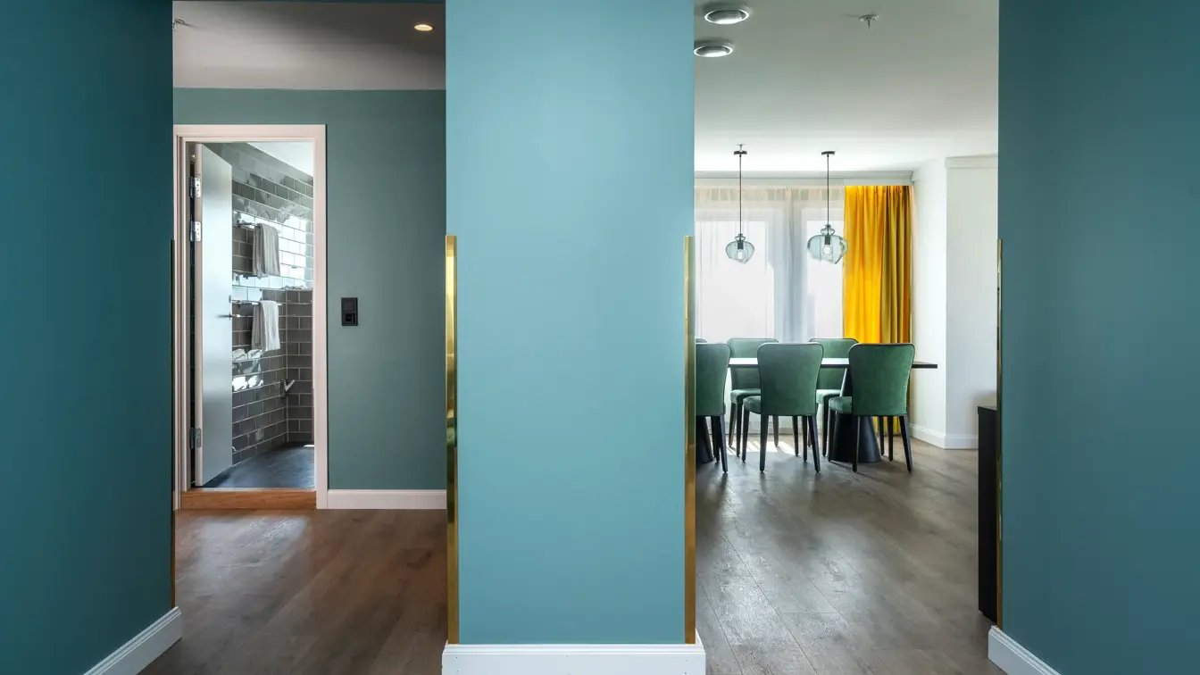 Grønn vegg, spisebord, 6 grønne stoler, vindu, gule gardiner, parkettgulv