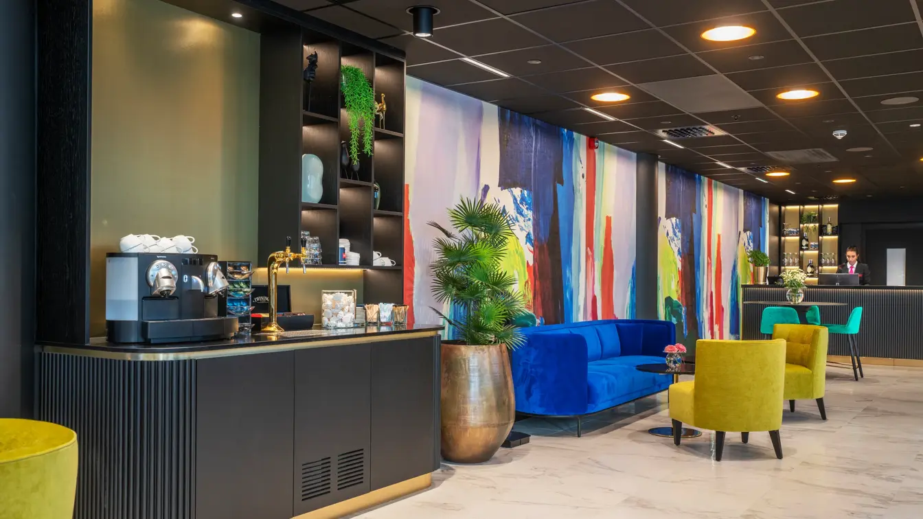 To gule lenestoler, salongbord, blå sofa. vegg i ulike farger, plante, kaffestasjon