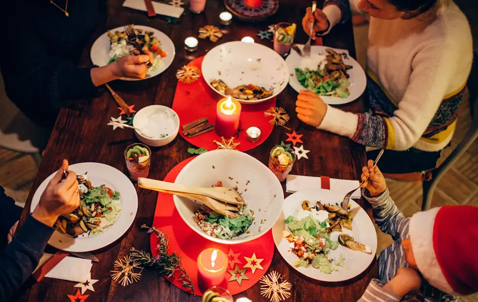 Folk som spiser vegetar julemiddag rundt et bord med rød duk