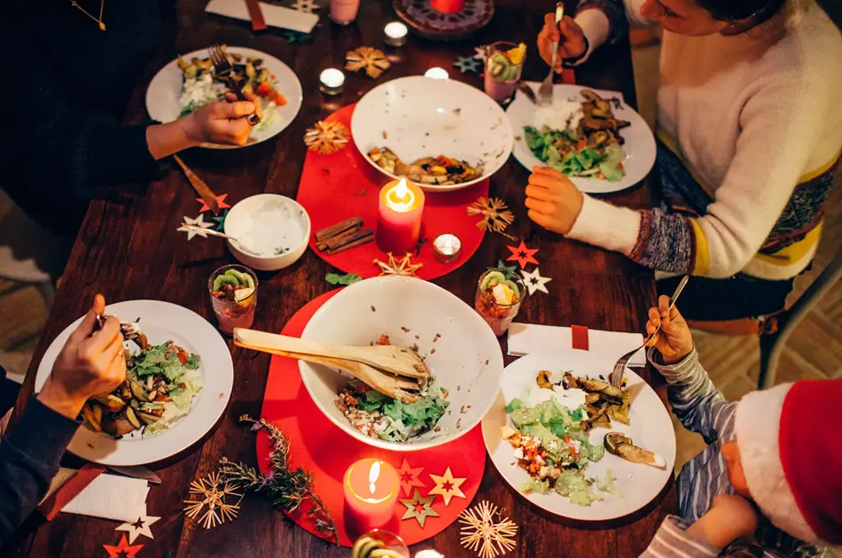 Folk som spiser vegetar julemiddag rundt et bord med rød duk