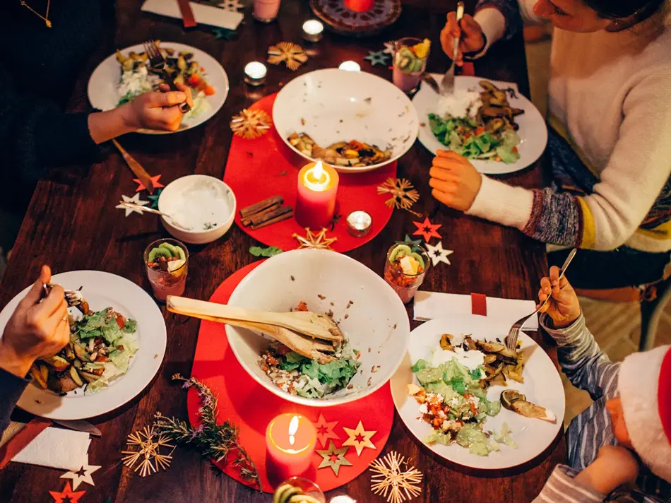 Folk som spiser vegetar julemiddag rundt et bord med rød duk
