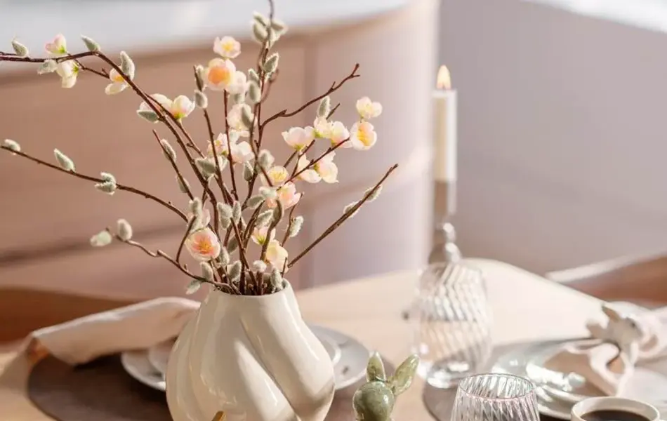 Dekket bord med kaninservise, vase med grener, kaninfigurer til pynt, glass, stearinlys, kaffekrus, servietter og serviettringer.