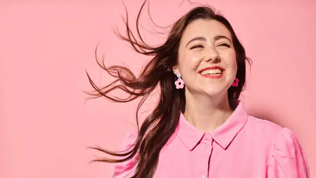 Dame som smiler med rosa skjorte, øredobber og bakgrunn