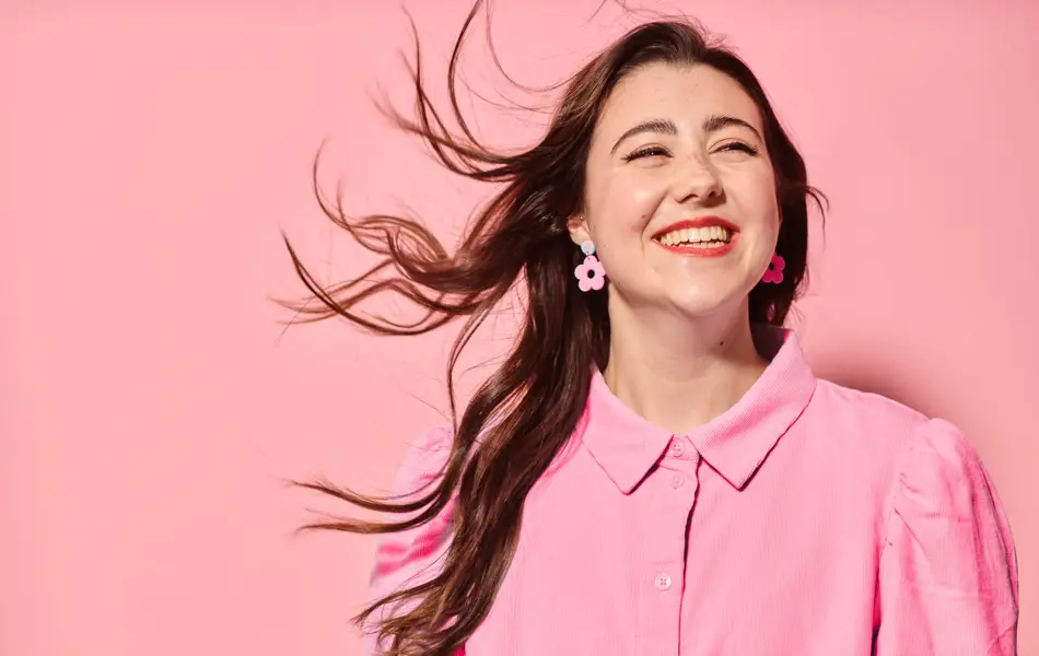 Dame som smiler med rosa skjorte, øredobber og bakgrunn