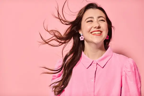 Dame som smiler med rosa skjorte, øredobber og bakgrunn