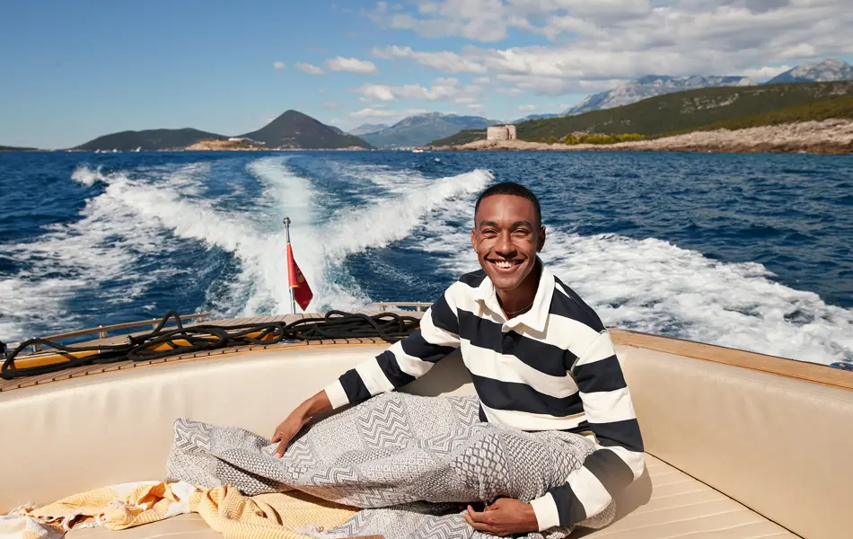 Mann med mørkeblå- og hvitstripete genser smiler til kamera sittende i en båt ute på vannet 