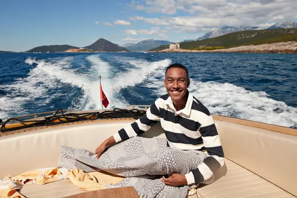 Mann med mørkeblå- og hvitstripete genser smiler til kamera sittende i en båt ute på vannet 