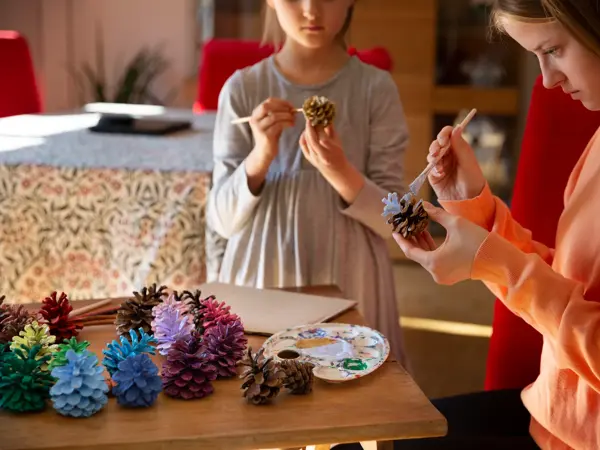 To jenter står og maler kongler 