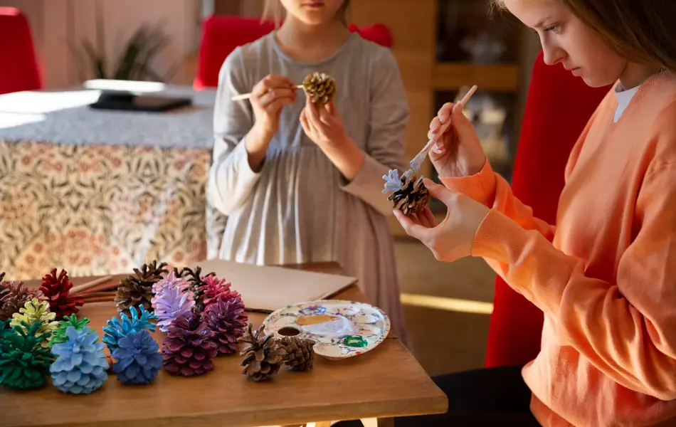 To jenter står og maler kongler 