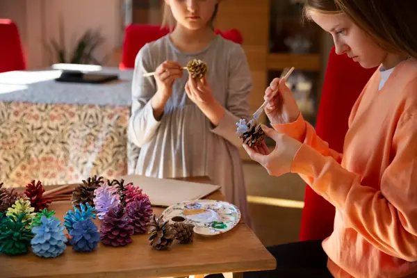 To jenter står og maler kongler 