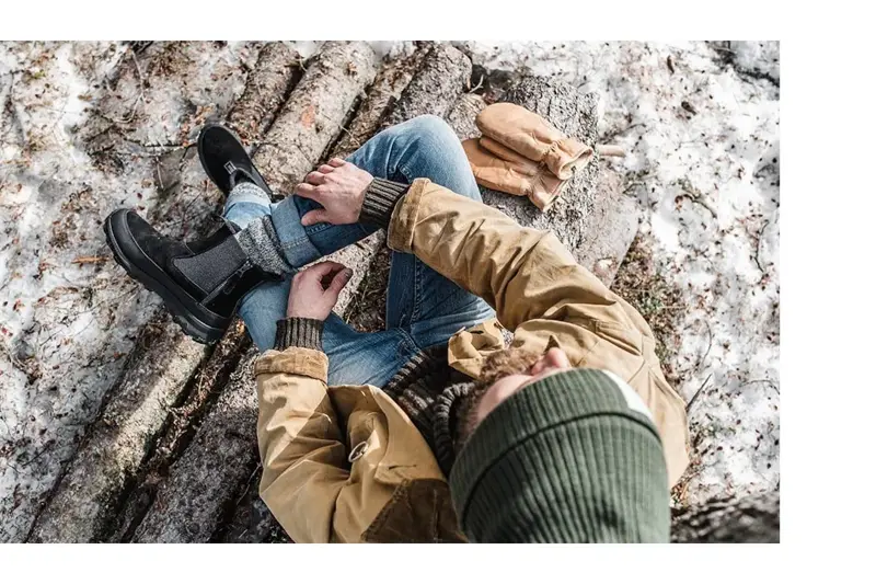 mann som sitter på en tømmerstokk ute på vinteren
