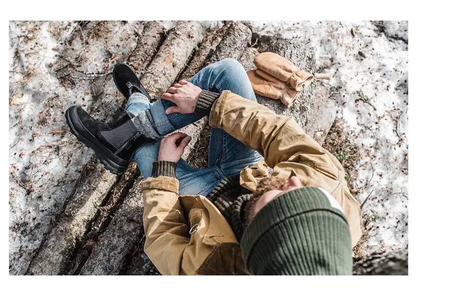 mann som sitter på en tømmerstokk ute på vinteren