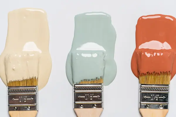 En dame som holder på med oppussing og tips om interiør trender for våren 2021. Damen har lyst halvlangt hå og har på seg en blå olaskjorte og blå olabukse. Fargene går i brunt og beige jordtoner og det er mye lilla og pastellfarger. Vårens interiør