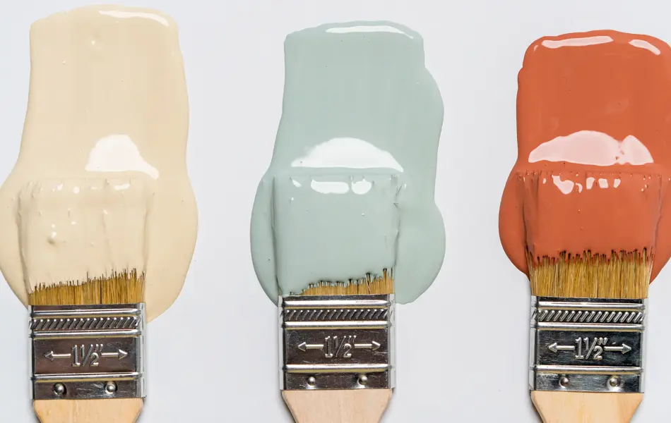 En dame som holder på med oppussing og tips om interiør trender for våren 2021. Damen har lyst halvlangt hå og har på seg en blå olaskjorte og blå olabukse. Fargene går i brunt og beige jordtoner og det er mye lilla og pastellfarger. Vårens interiør