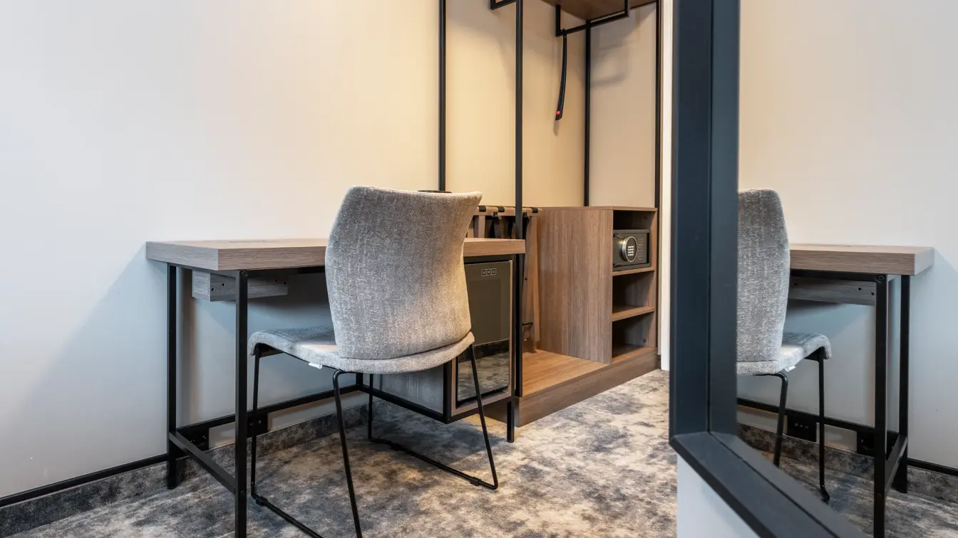 Standard rom med skrivebord og tilhørende stol, med åpen garderobe og teppegulv.