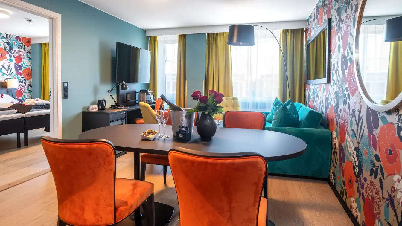 Blomstertapetvegg, TV, vindu, turkis sofa, salongbord, gule stoler, spisebord, oransje stoler, veggspeil, gulvlampe , parkettgulv