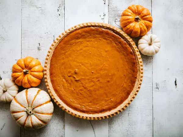 A high angle view looking down on a freshly baked pumpkin pie, just in time for your autumn or Thanksgiving season celebration.  Small decorative gourds decorate the scene.  Horizontal image with copy space.