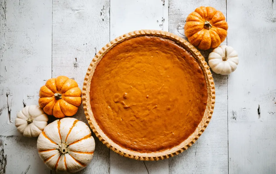 A high angle view looking down on a freshly baked pumpkin pie, just in time for your autumn or Thanksgiving season celebration.  Small decorative gourds decorate the scene.  Horizontal image with copy space.
