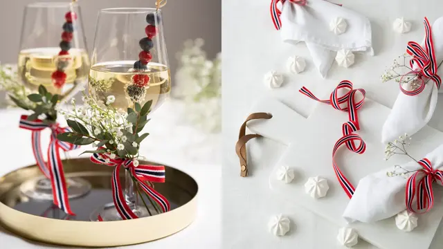 To vinglass pyntet med 17.mai-bånd og blomster. Hvit duk med hvite servietter med 17.mai-bånd og hvite marengs på bordet.