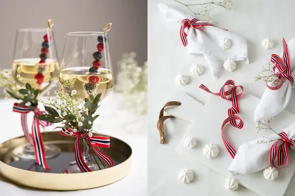 To vinglass pyntet med 17.mai-bånd og blomster. Hvit duk med hvite servietter med 17.mai-bånd og hvite marengs på bordet.