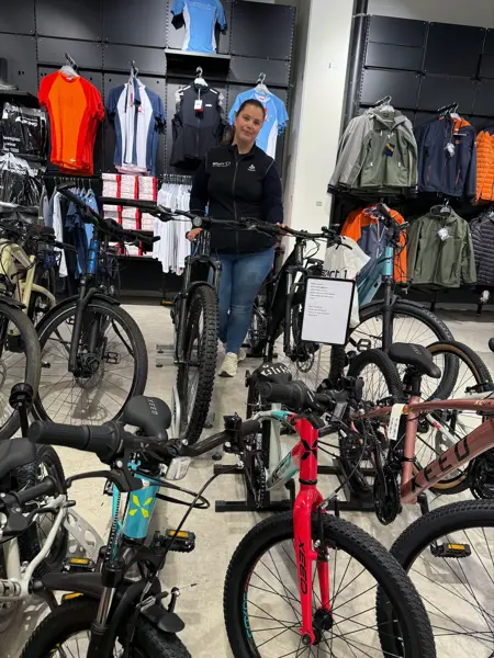 Dame som smiler og viser frem sykler i butikken