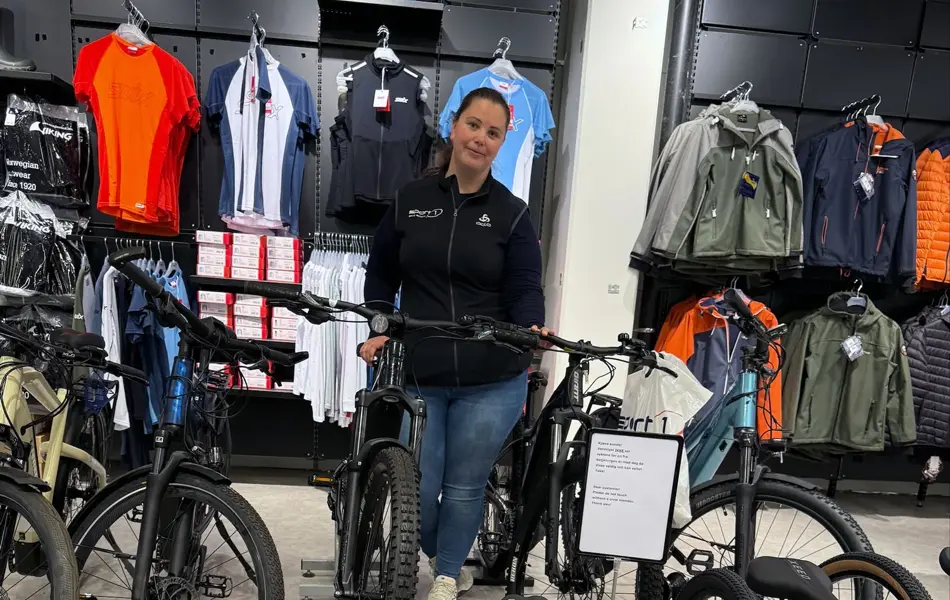 Dame som smiler og viser frem sykler i butikken