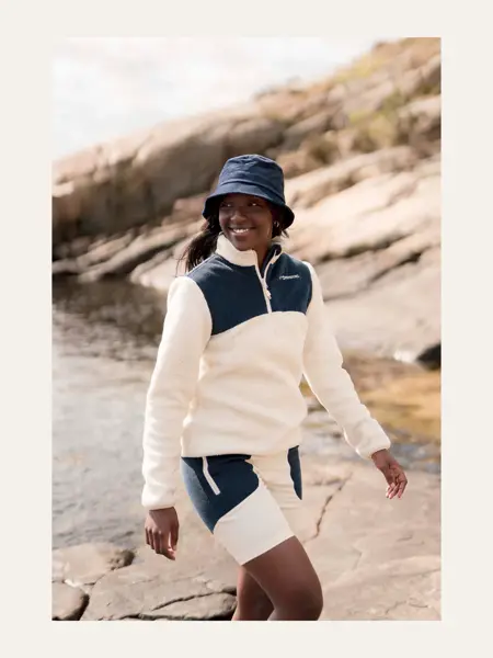 dame på svaberg med blå bøttehatt, hvit og blå fleecegenser og shorts.