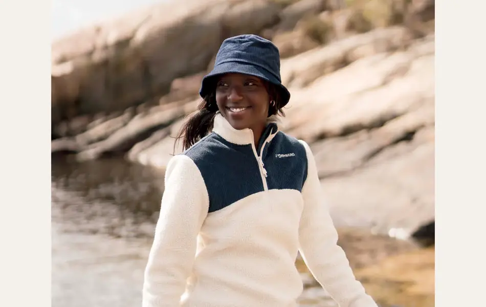 dame på svaberg med blå bøttehatt, hvit og blå fleecegenser og shorts.