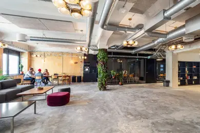 Interiør fra kontoret til The Oslo Company, stor og åpen sosial sone med rustikke detaljer som betonggulv og ventilasjon, grønne planter og lyse farger på veggene