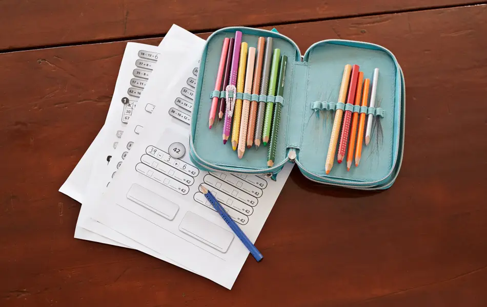 grønn pennal med fargeblyanter som ligger oppå skoleoppgaver