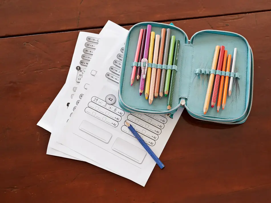 grønn pennal med fargeblyanter som ligger oppå skoleoppgaver