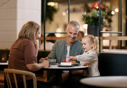 En mann, en kvinne og et barn sitter ved et bord på en kafé, mannen og kvinnen smiler til barnet