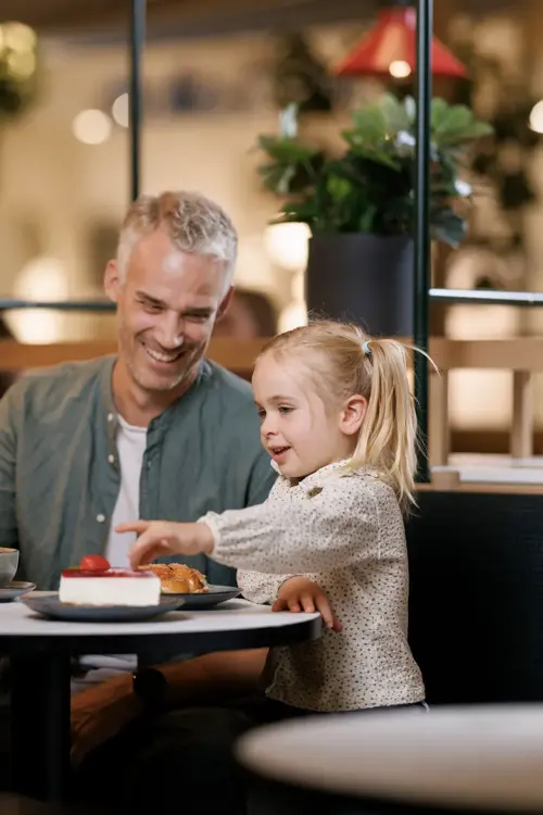 En mann, en kvinne og et barn sitter ved et bord på en kafé, mannen og kvinnen smiler til barnet