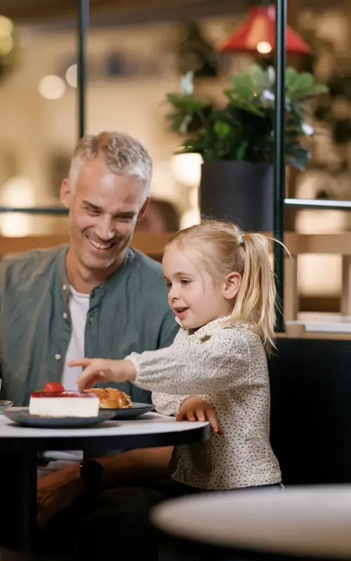 En mann, en kvinne og et barn sitter ved et bord på en kafé, mannen og kvinnen smiler til barnet