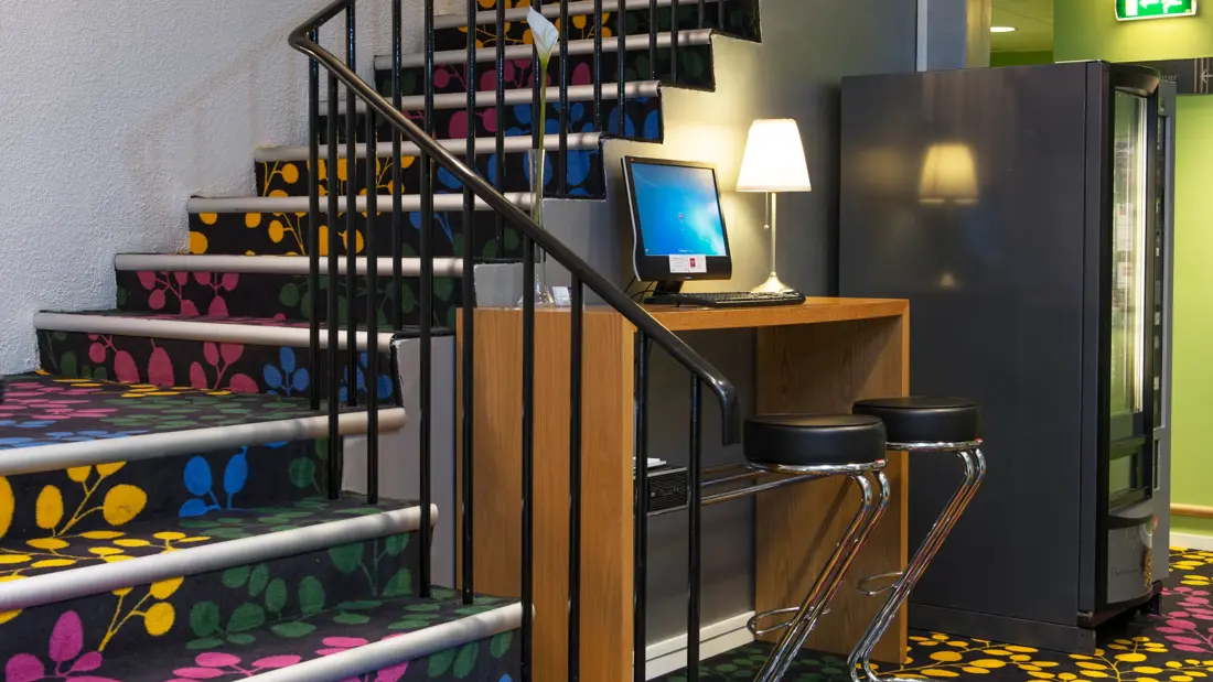 Trappeoppgang fra resepsjonen til etasjene over. Trappen er kledd i et fargerikt teppe med gule, blå, grønne og rosa blader.