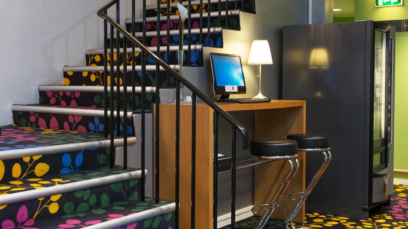 Trappeoppgang fra resepsjonen til etasjene over. Trappen er kledd i et fargerikt teppe med gule, blå, grønne og rosa blader.