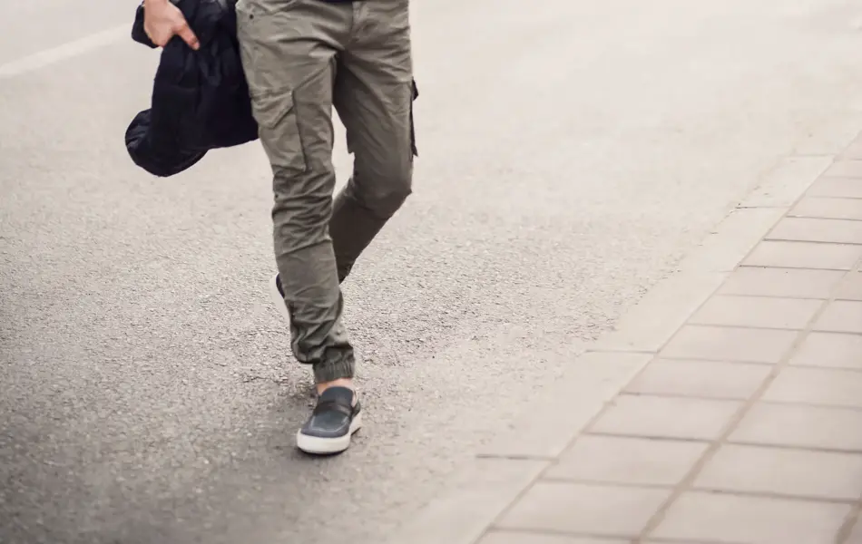 Mann gående over gata iført grønn cargobukse, svart t-skjorte og solbriller.