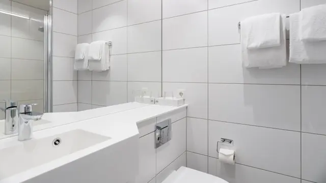 Flislagt bad med håndklær på veggen, og servant med speil over.