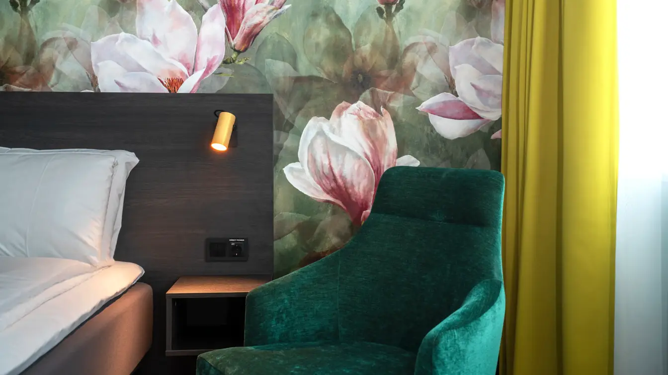 Blomstertapet, seng, grønn lenestol, gule gardiner 